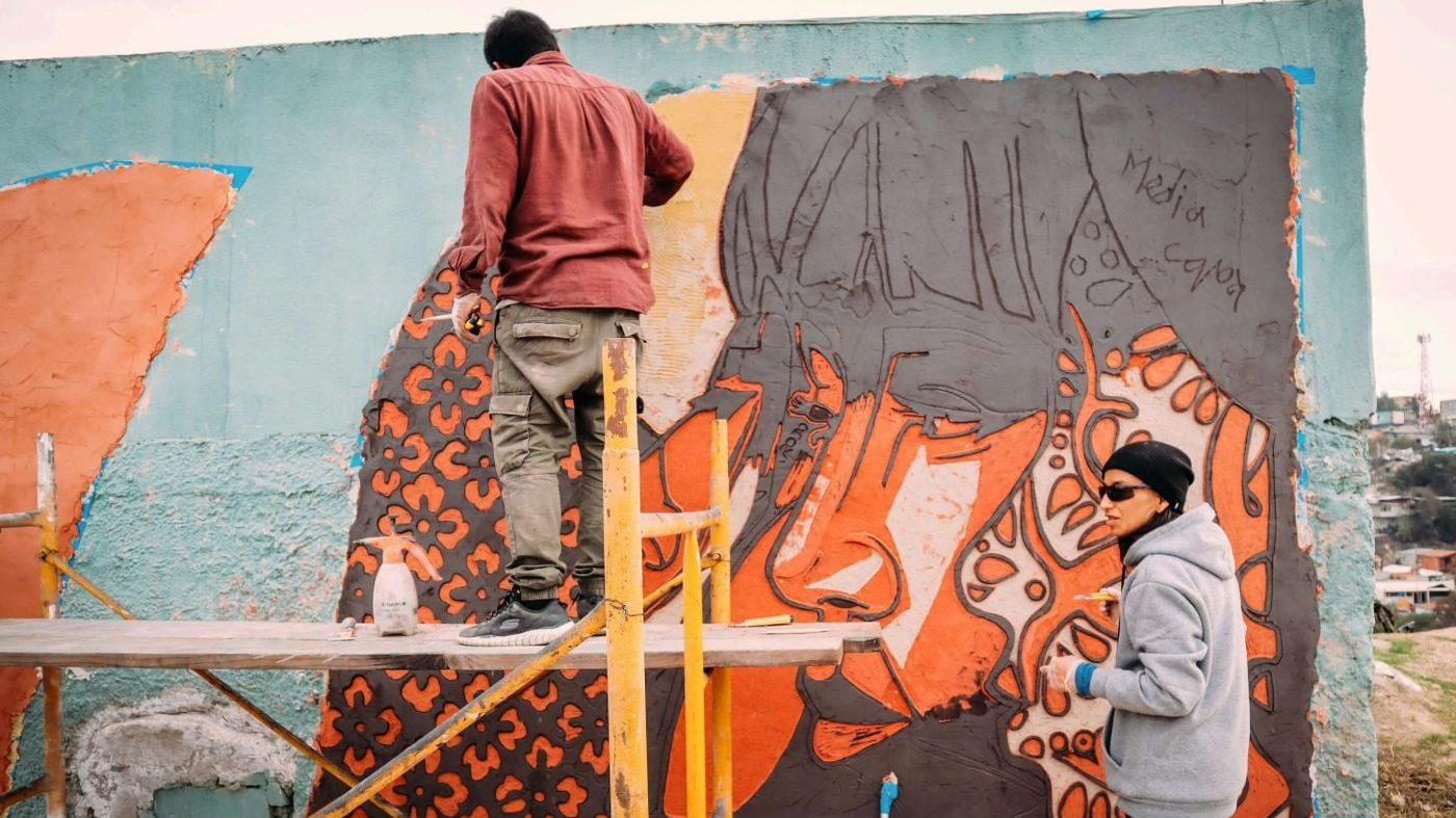 Dos personas pintan un muro desde un andamio