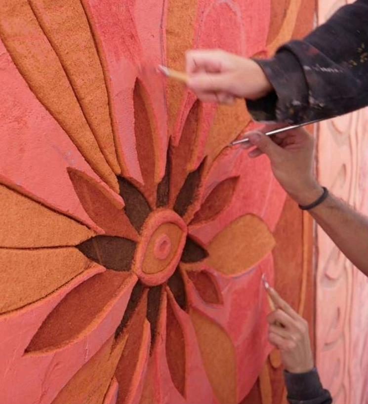Manos tallando una flor en un muro rosa